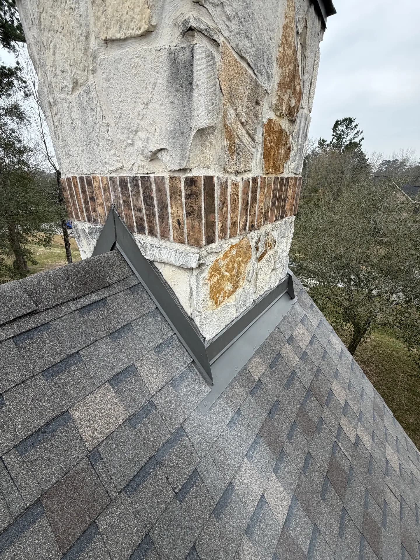 Stone chimney and metal flashing at the roofline, the same area where a chimney cap protects the flue opening