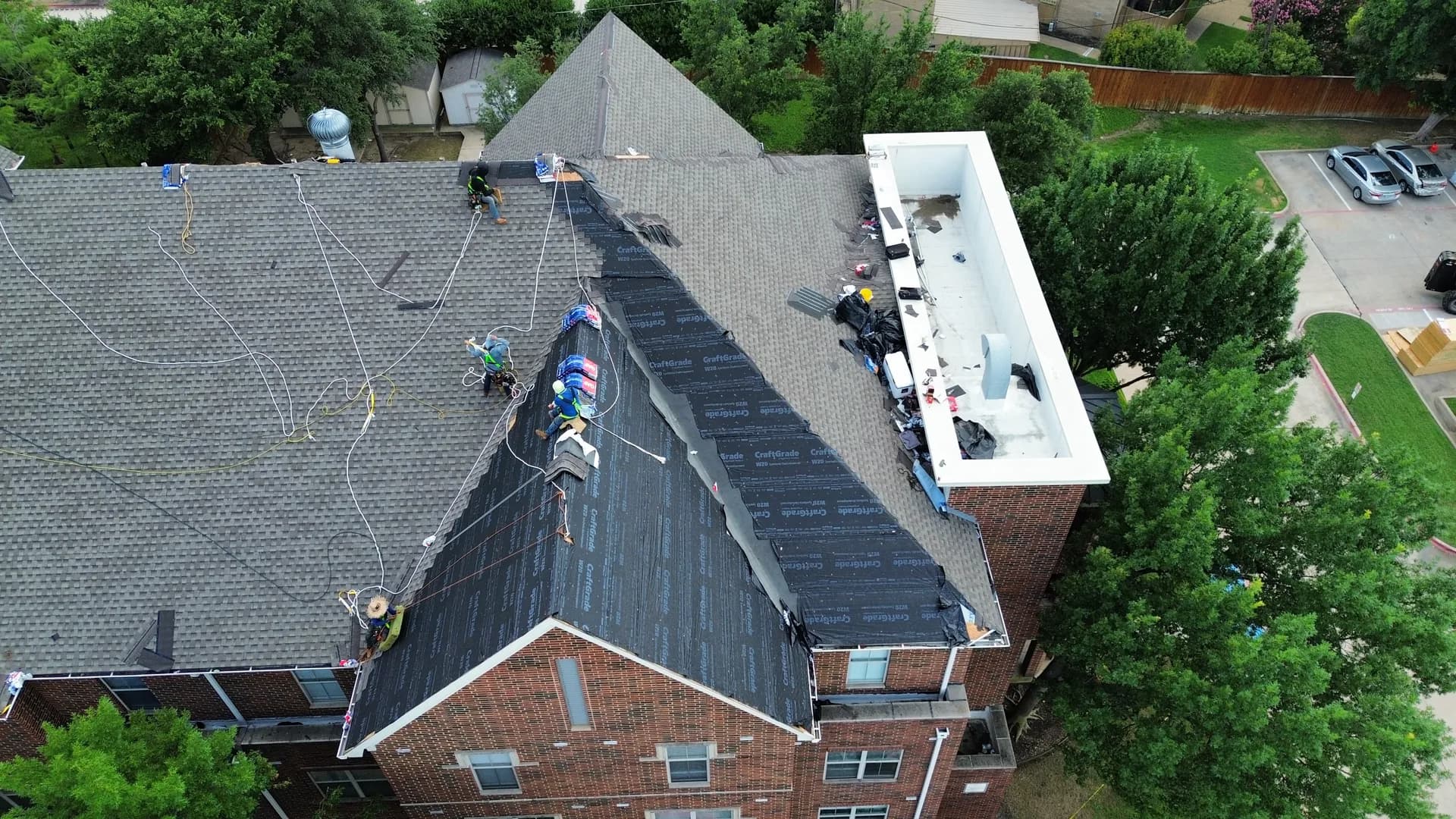 ROYH Build Co roofing crew in safety harnesses repairing a section of a commercial building's roof, with a flat TPO membrane area visible alongside the work zone