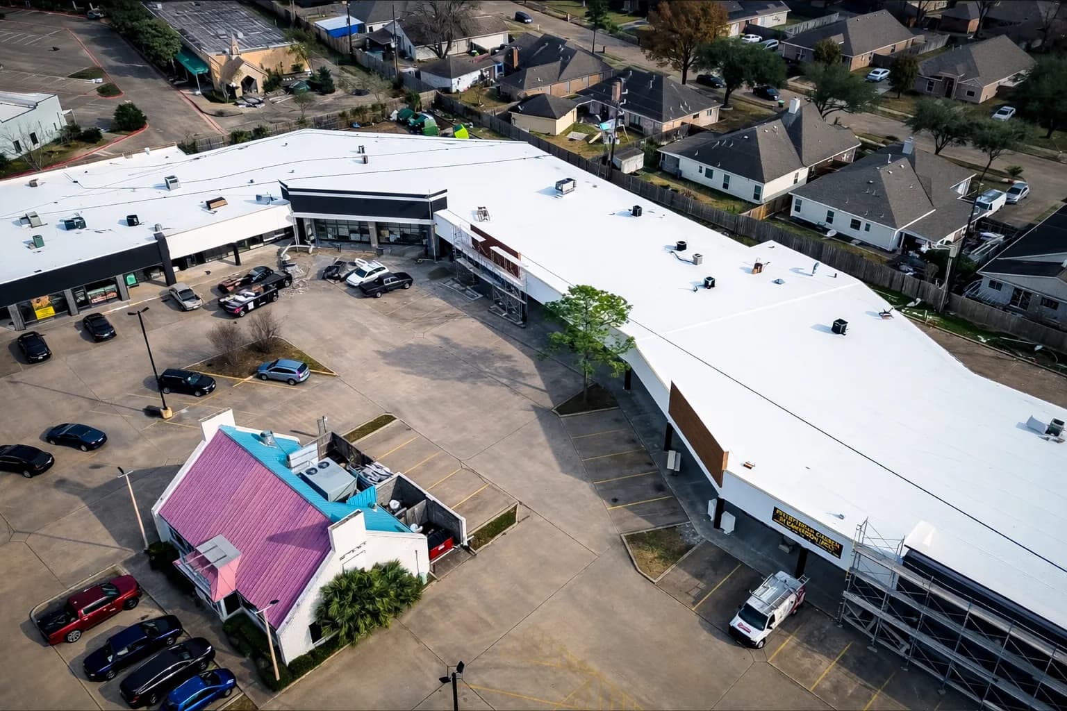 Aerial drone view of a white TPO single-ply commercial roof installation with a colorful restaurant building visible in the parking lot below