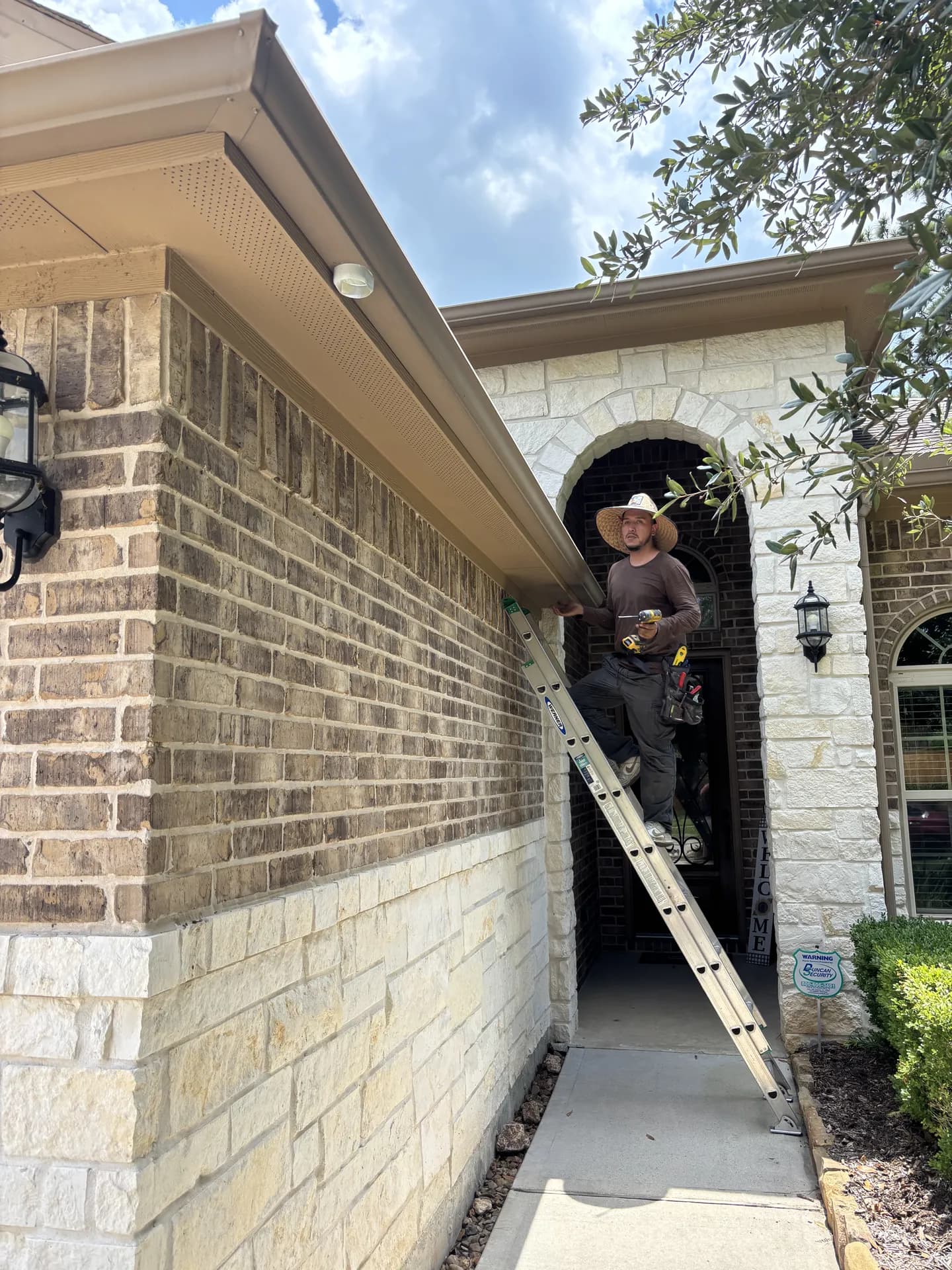 ROYH Build Co crew member installing a Senox seamless gutter system along a stone and brick home exterior near The Woodlands, TX
