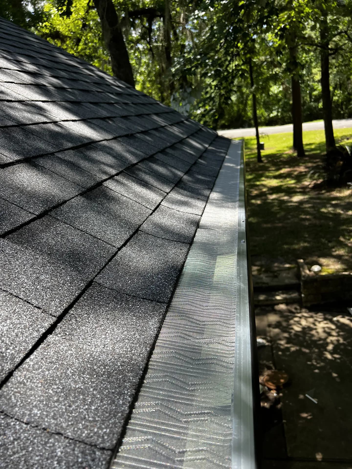 Close-up angled shot down a shingle roof slope showing a newly installed gutter with mesh guard along the eave, representative of gutter protection on a Houston-area home.