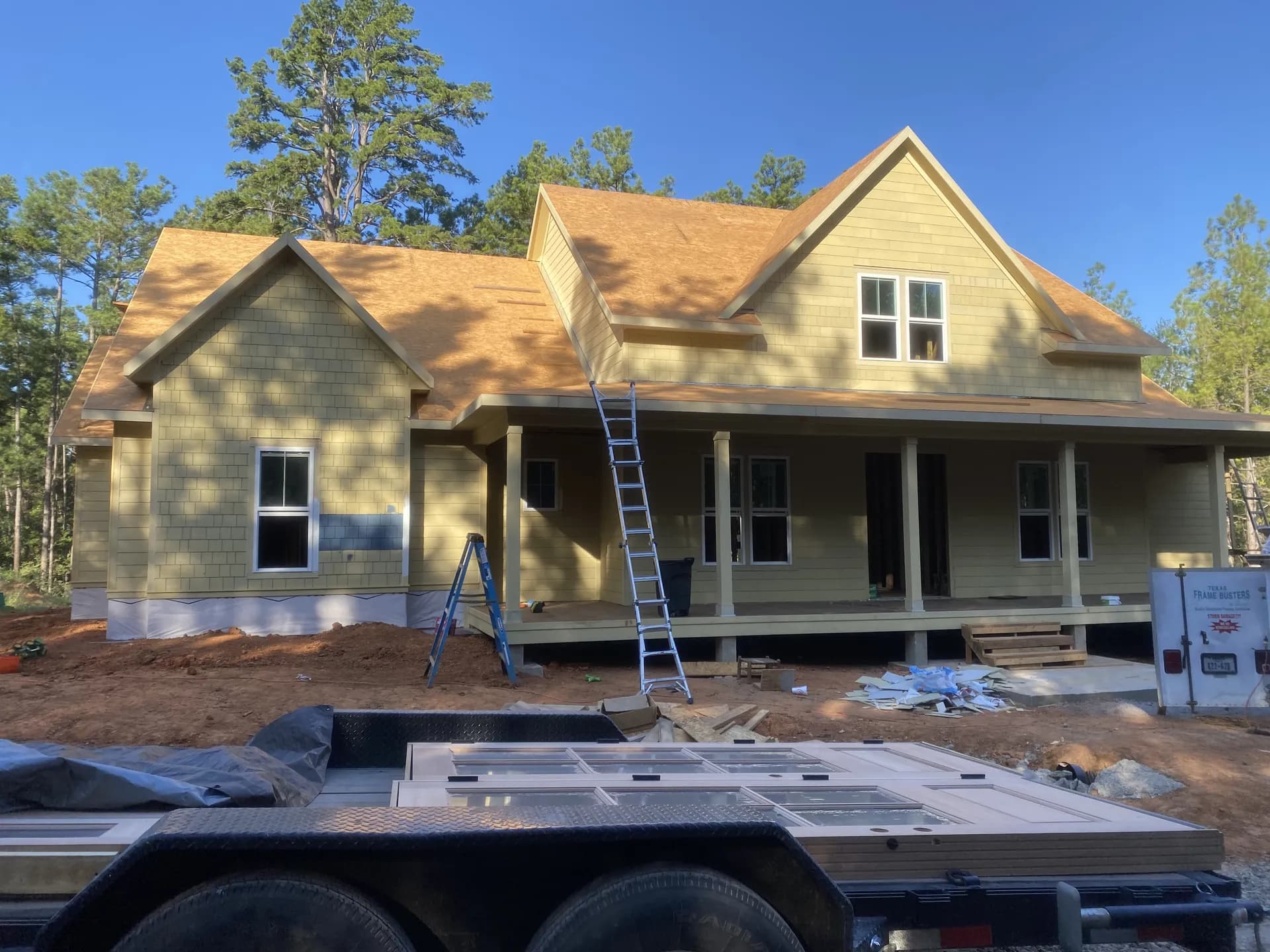 Two-story custom home under construction near The Woodlands, TX with roof decking installed and the front porch taking shape ahead of new roof installation