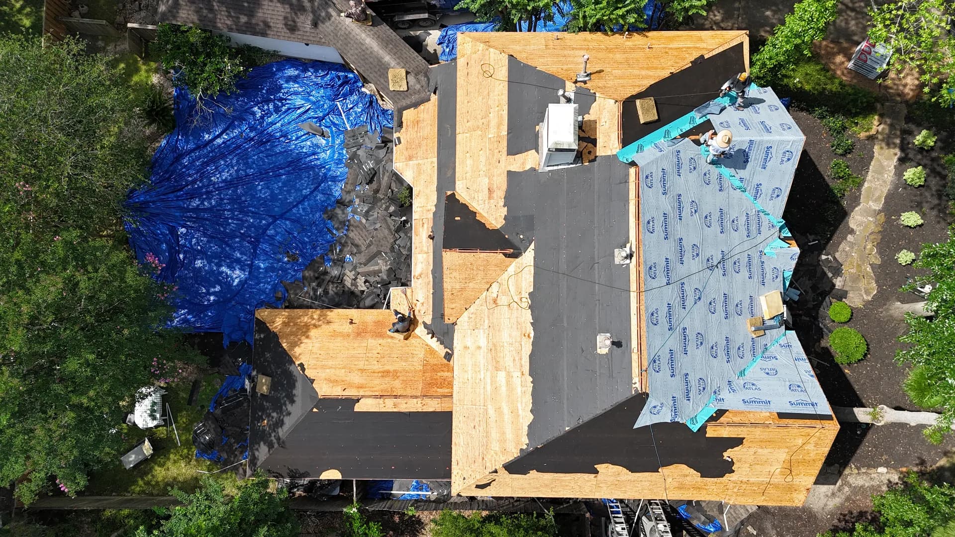 Aerial view of a roof tear-off in progress down to the decking, with old shingles removed and new underlayment partially installed