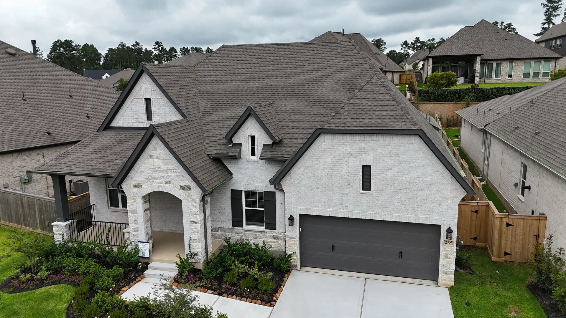 Ground-level front elevation of a finished stone and brick home with a new tan dimensional shingle roof and manicured landscaping