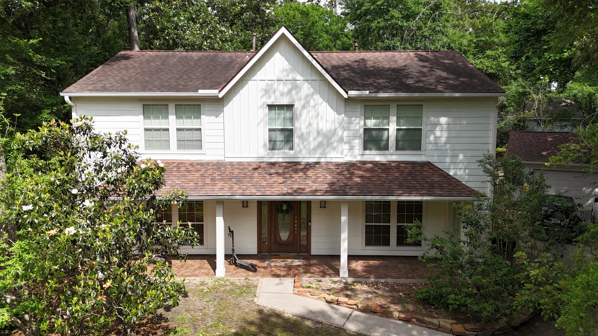 Front elevation of a white two-story home with a completed brown architectural shingle roof over the main roofline and covered porch after a finished roof replacement.
