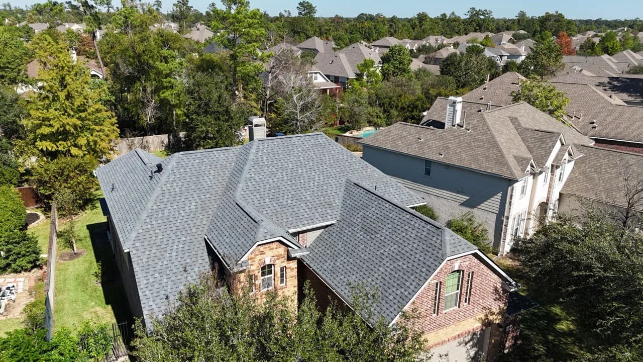 Aerial drone view of a large gray composition shingle roof on a home surrounded by neighborhood trees