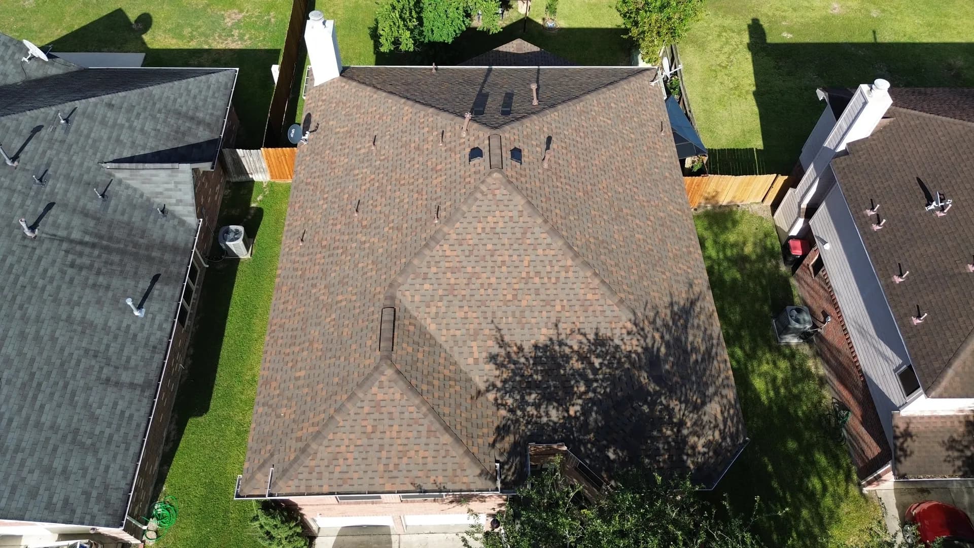 Aerial view of a brown dimensional shingle roof with a complex hip and valley design and visible ridge vents installed along the peak near The Woodlands, TX
