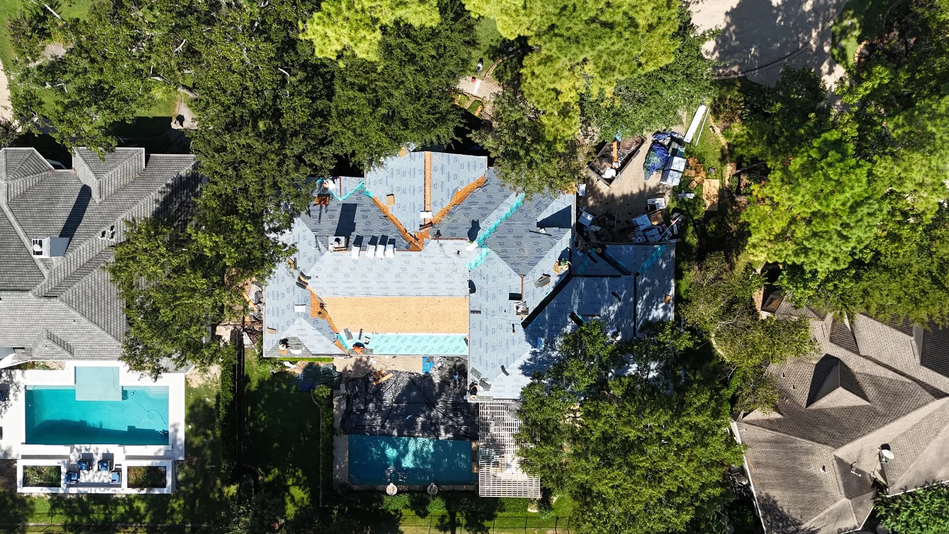 Aerial view of a finished gray dimensional shingle roof on a tree-shaded home with two pools in the yard