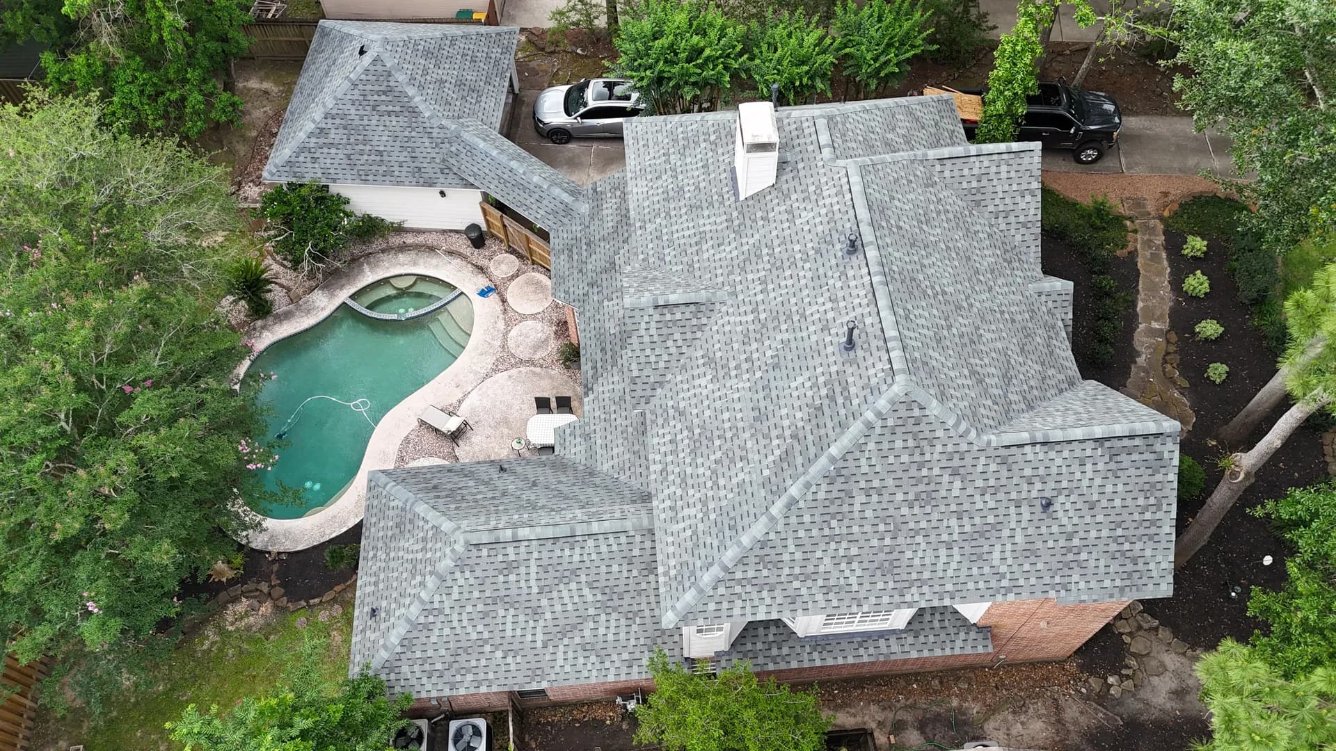Aerial view of a finished gray architectural shingle roof on a large home with a curved pool and hot tub in the side yard