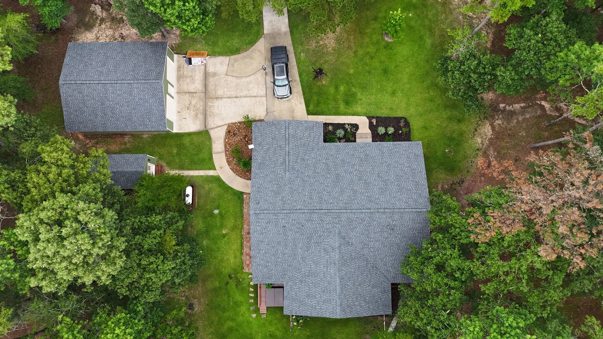 Wide aerial view of a residential rooftop and surrounding yard