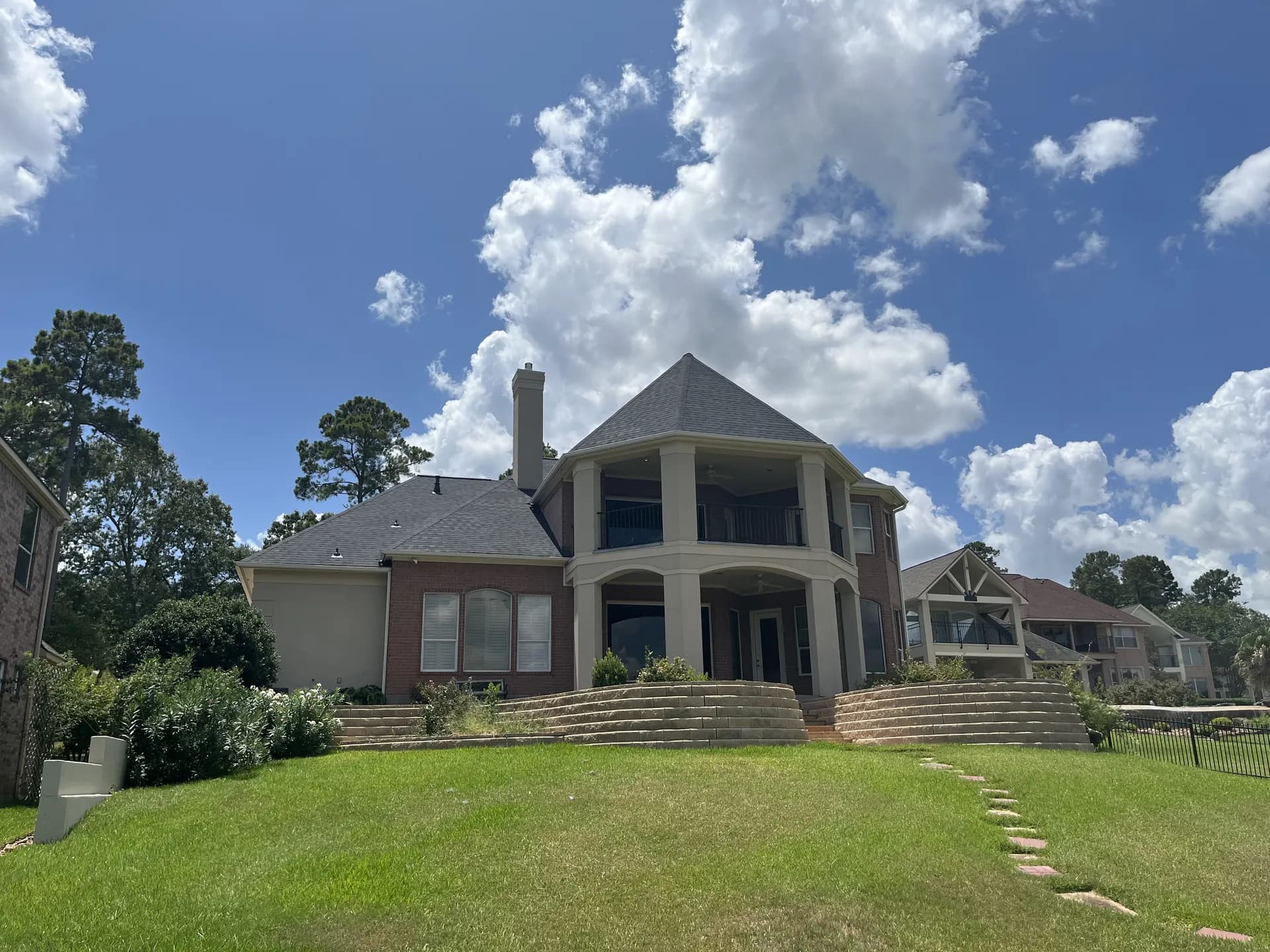 Wide front view of a large two-story stucco and brick home with a new gray composition shingle roof and a turret