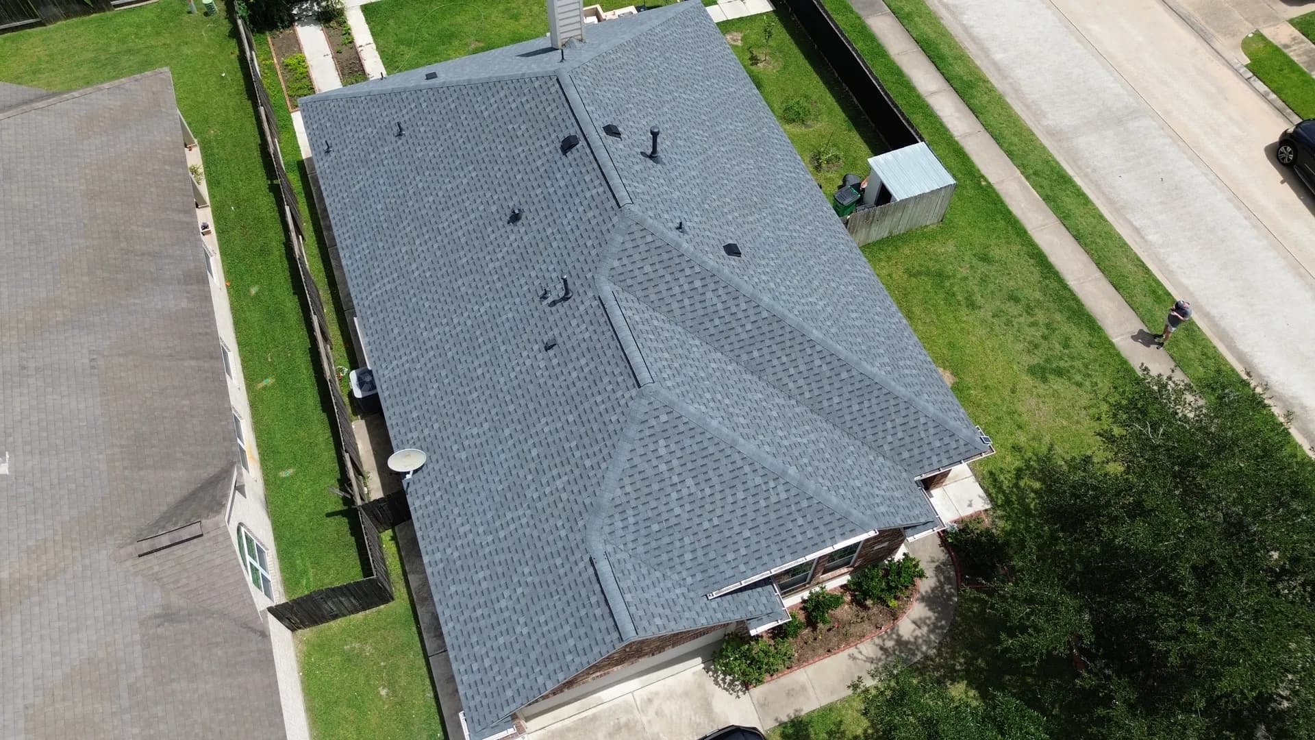 Aerial drone view of a completed gray shingle roof on a home with a chimney, with an adjacent building visible