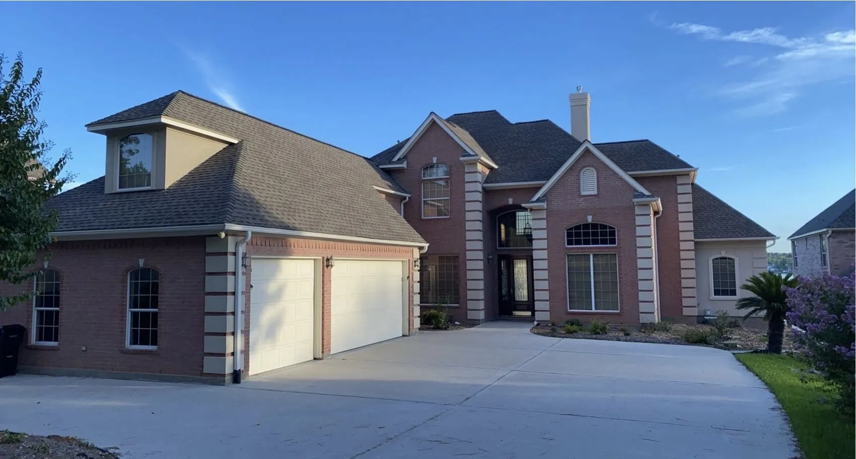 Large brick two-story home with a completed new composition shingle roof and a three-car garage, photographed at dusk