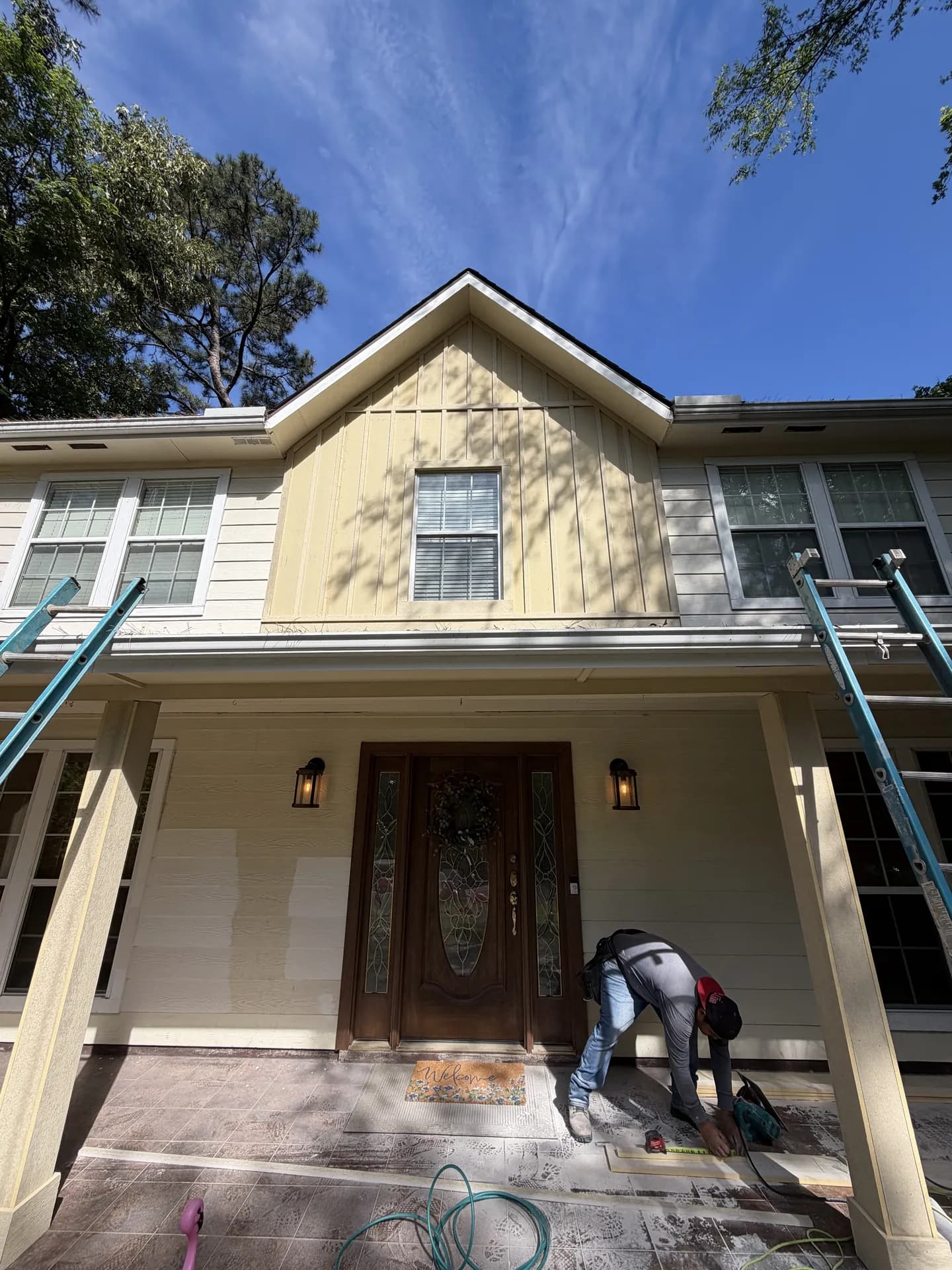 ROYH Build Co crew member finishing trim work at a Texas home's front entry during a siding repair, with ladders positioned against the gable