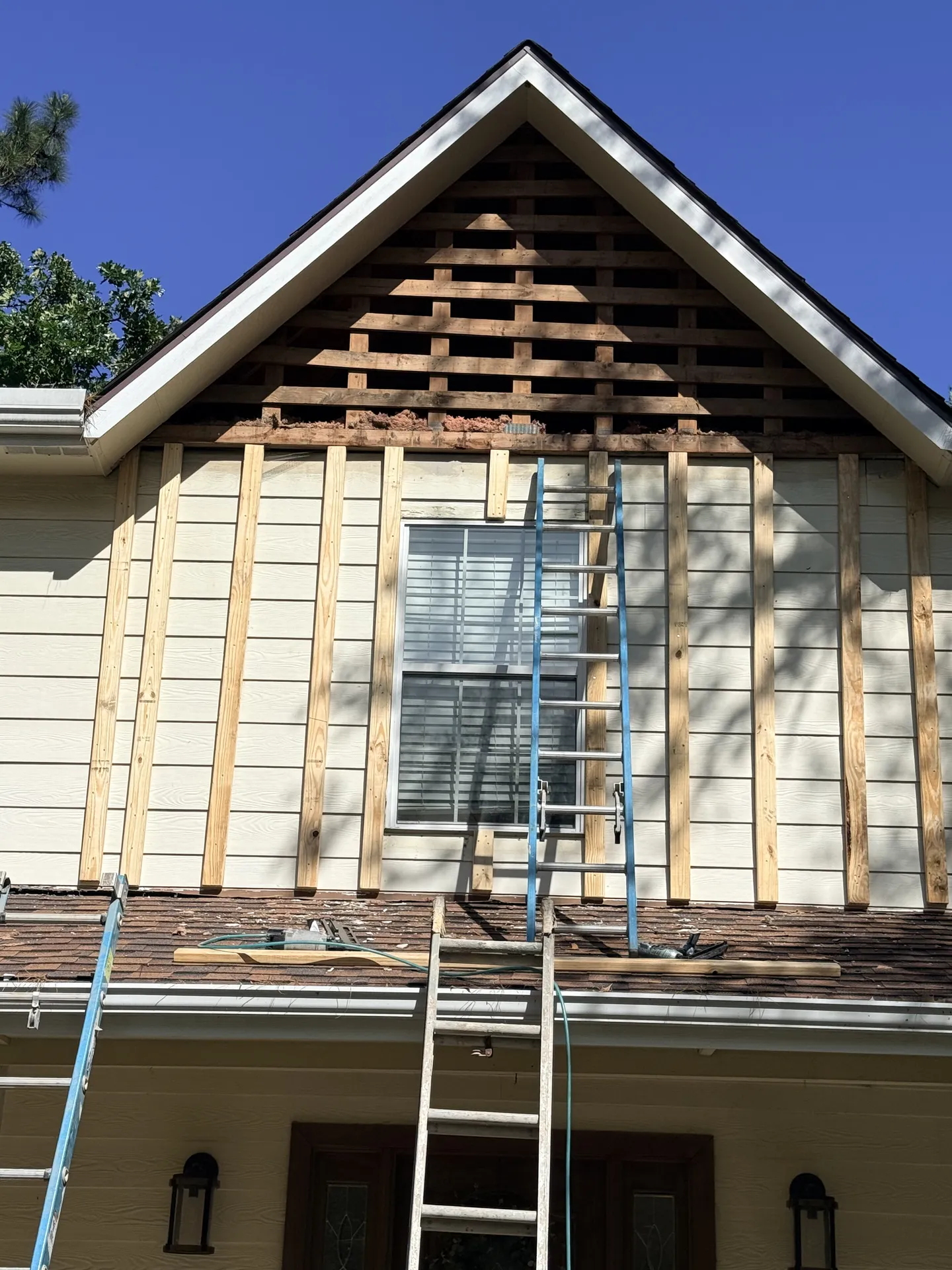 Fiber cement siding installation in progress on a gable end, showing new panels fastened over house wrap with trim boards ready for finishing