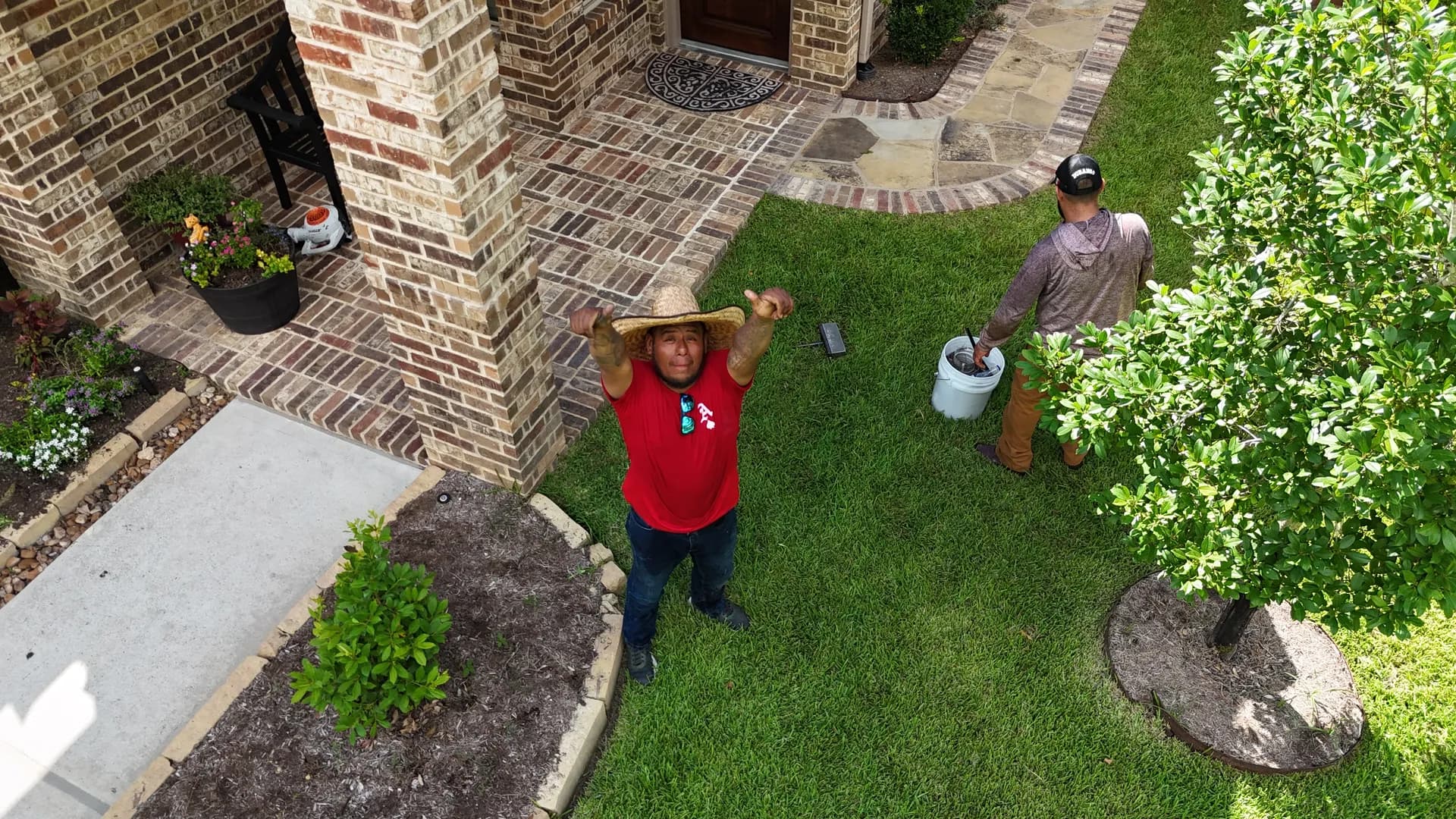 Two ROYH Build Co crew members in a client's yard, one in a straw hat looking up at the camera
