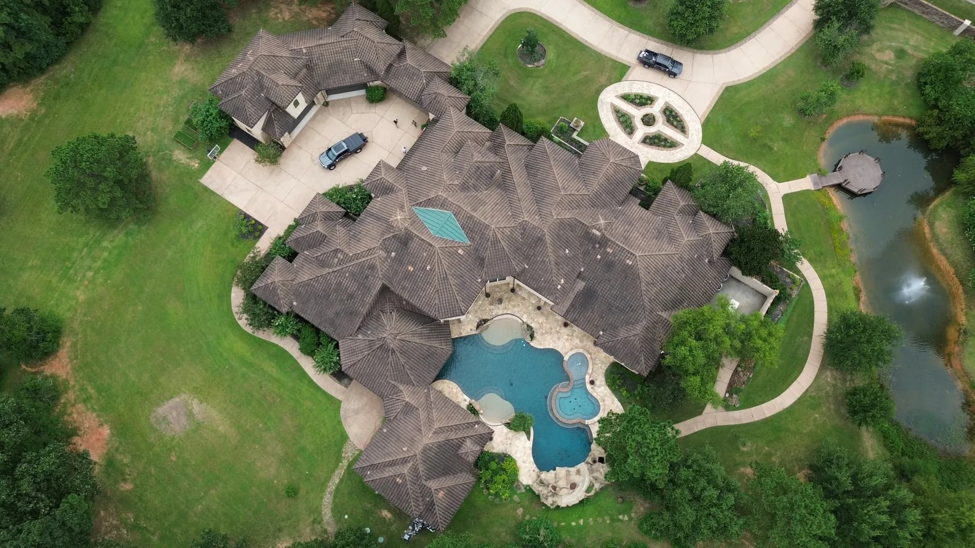 Straight-down aerial view of a concrete tile roof installed by ROYH Build Co on a luxury estate near The Woodlands, TX, with a circular motor court and two swimming pools below